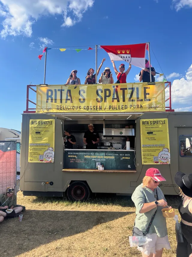 Rita's-Spätzle-Truck mit Fahnen, Gäste feiern auf dem Dach