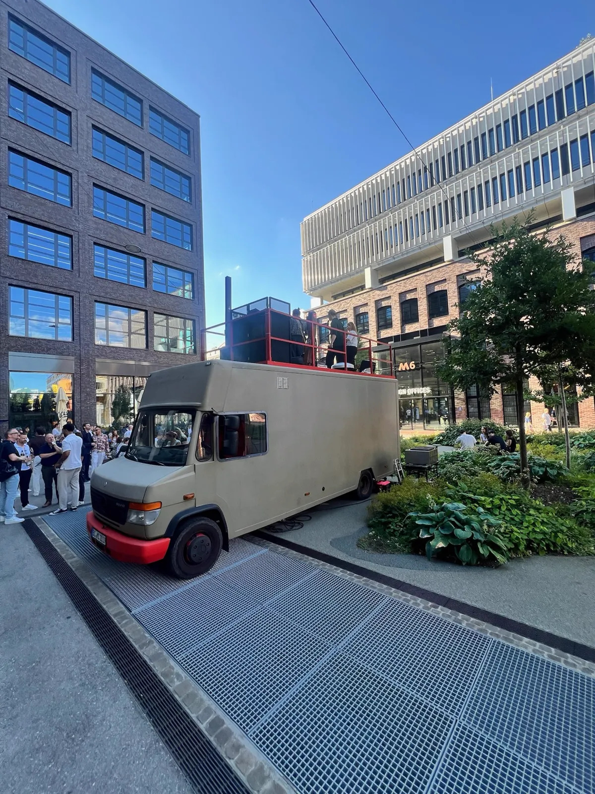 Der Häge Rooftop-Foodtruck vor modernen Bürogebäuden, Gäste stehen auf der Dachterrasse
